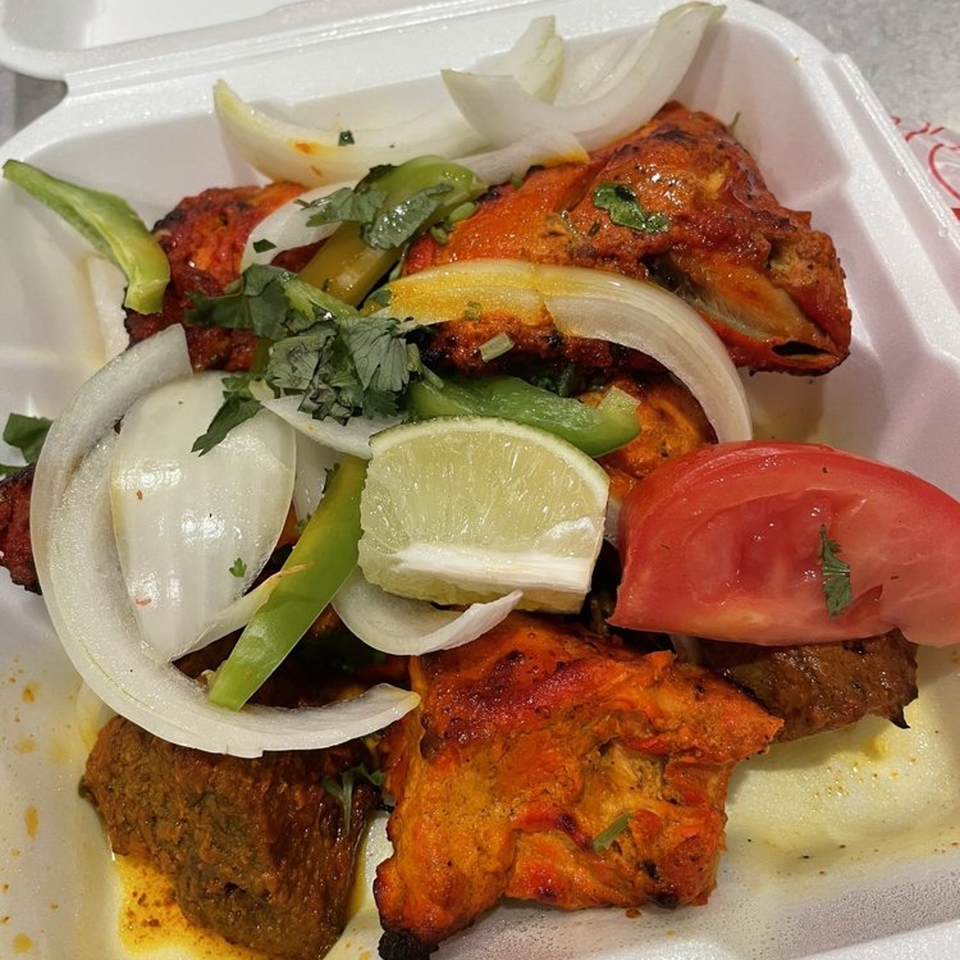 Assam Indian Kitchen's tandoori chicken with onions, peppers, lime, and tomato in a takeout container.