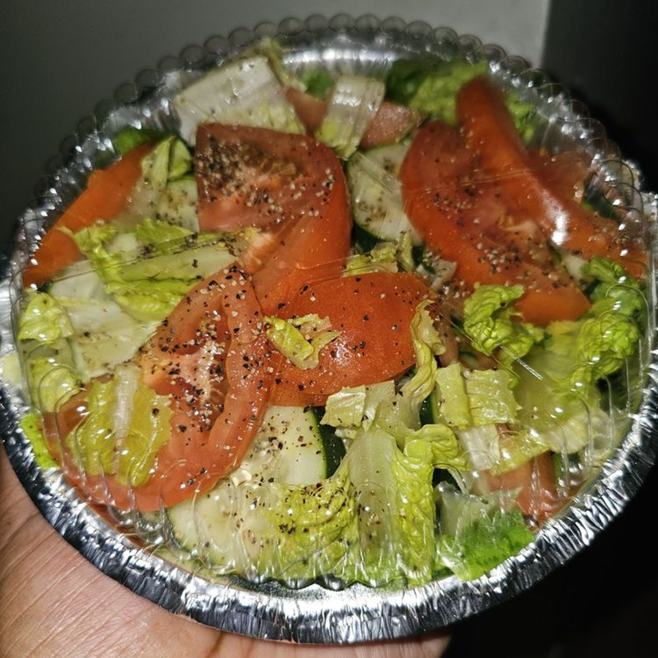Fresh garden salad with lettuce, tomatoes, and cucumbers, seasoned with pepper, in a foil takeout container.