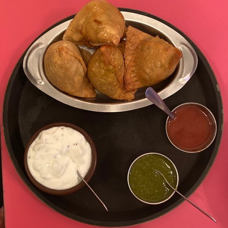 A platter of golden-brown samosas with three dipping sauces: red, green, and white.