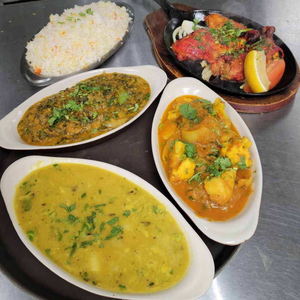 Assam Indian Kitchen's spread of Indian dishes: tandoori chicken, rice, saag, dal, and aloo gobi.