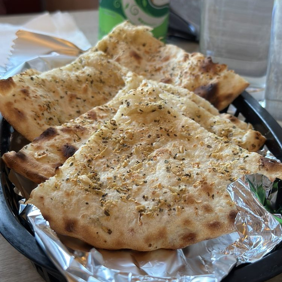 Several pieces of warm, seasoned Indian naan bread in a black basket lined with foil.